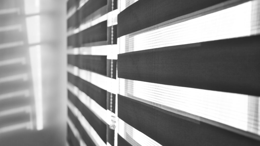 sun shining through window blinds throwing shadows wall black white